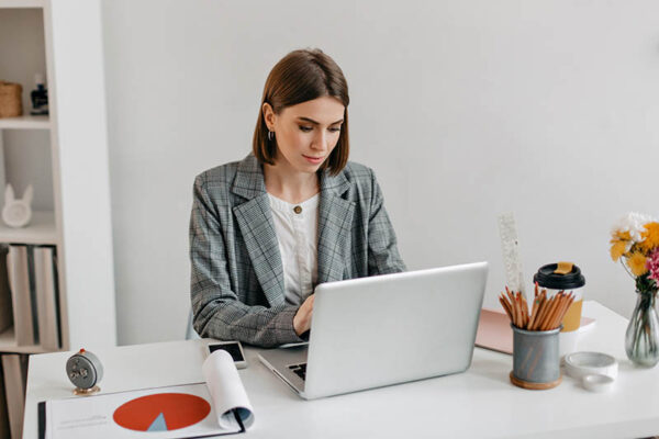 Business lady in gray jacket working in laptop. Portrait of woman in office.